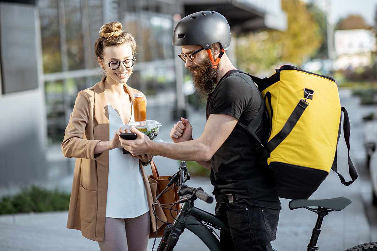 Courier delivering fresh lunches to a young business woman on a bicycle