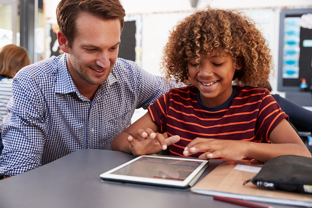 Teacher and schoolboy using digital tablet in class