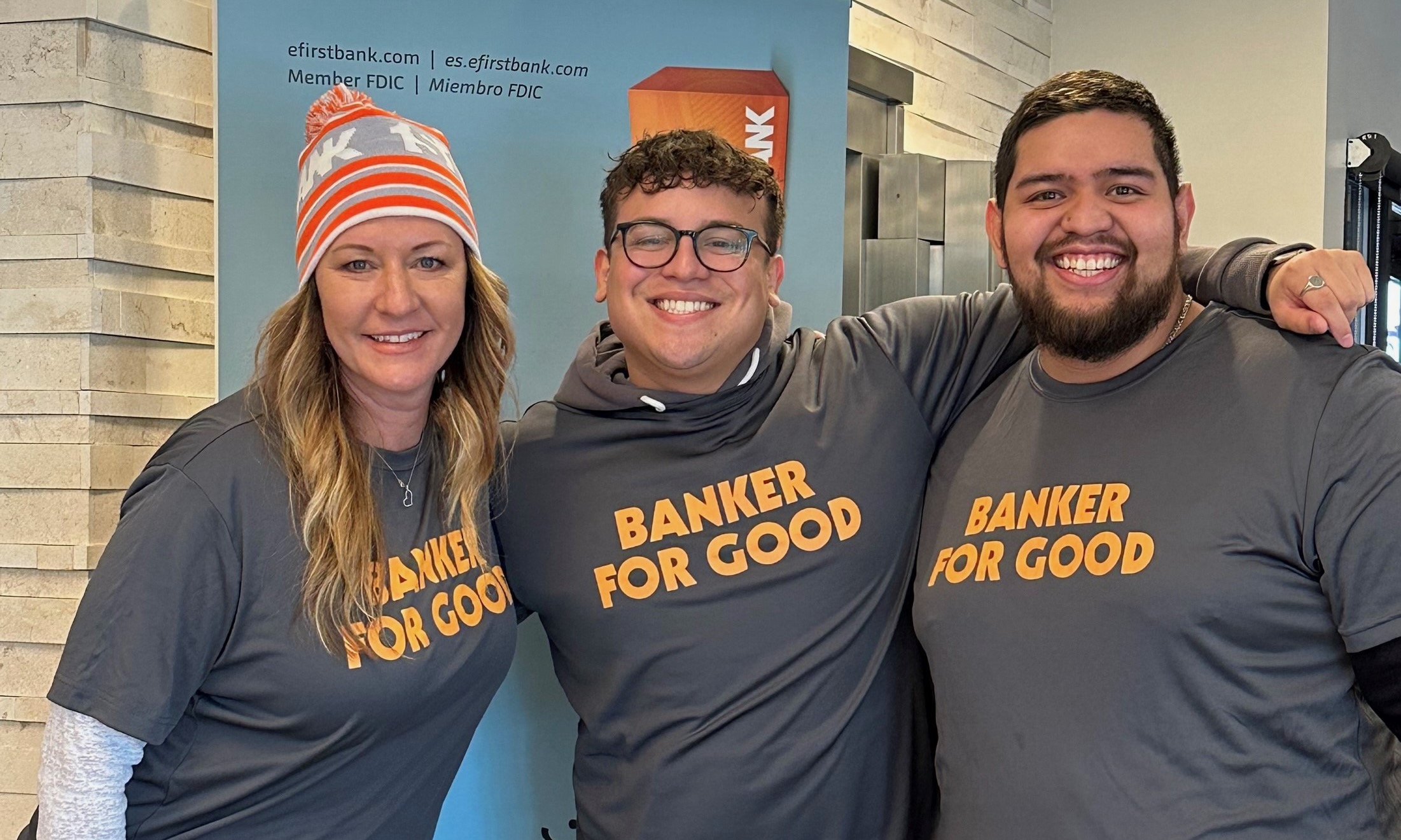 Three FirstBank team members pose for group picture wearing “Banker for Good” t-shirts.