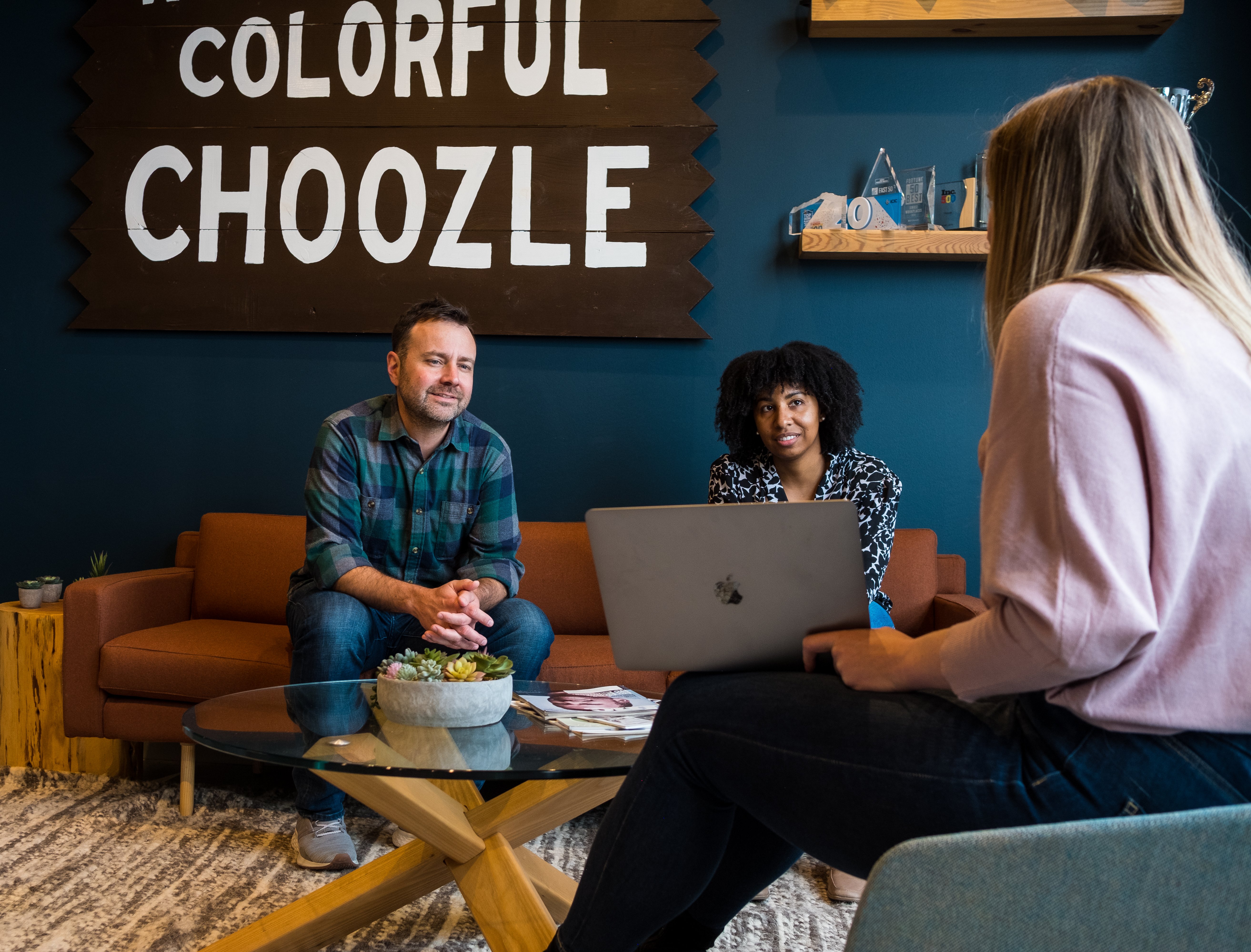 Three people — two on a couch and one on a chair — having a conversation around a small table in Choozle's office.