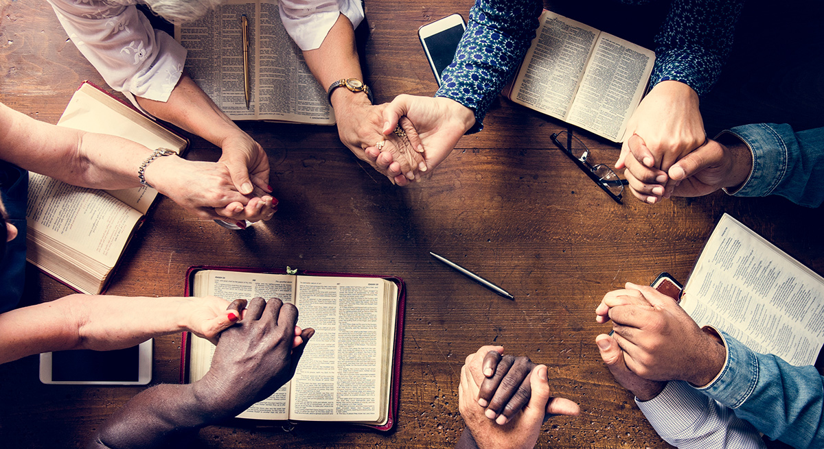 Group of people sitting around a table holding hands praying