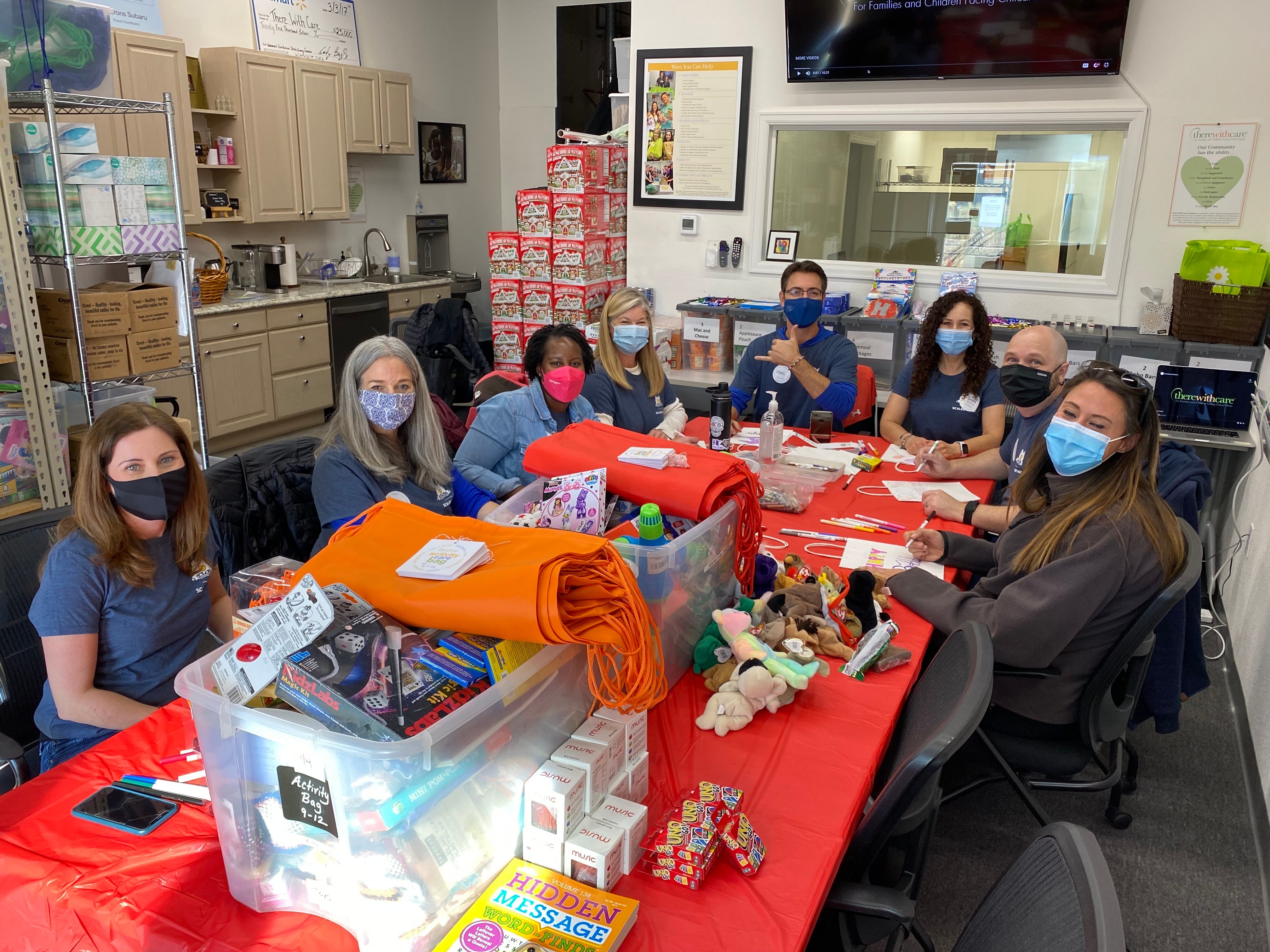 A group of individuals sitting around a table in masks, working on gifts for children.