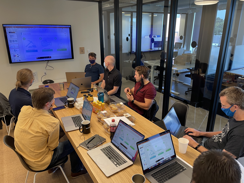 Members of the VIZIO team sitting around a meeting table, looking at a screen mounted on the wall with a Powerpoint on it.