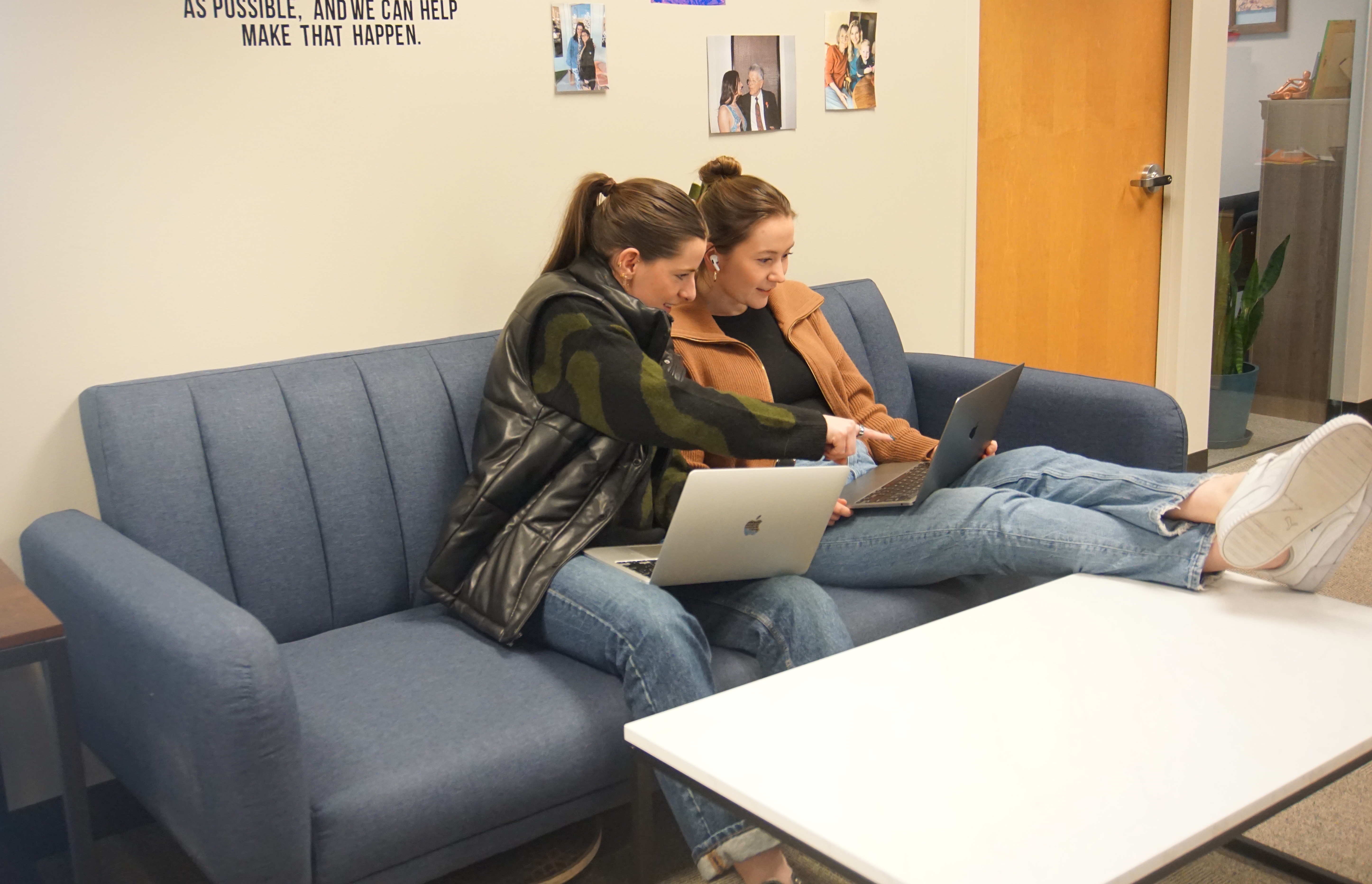 Two Nymbl Science co-workers sit on a couch, one with feet up, looking at a laptop