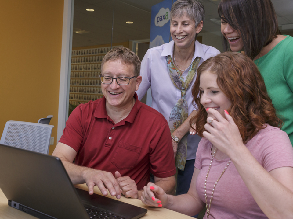 Pax8 employees gather around a computer