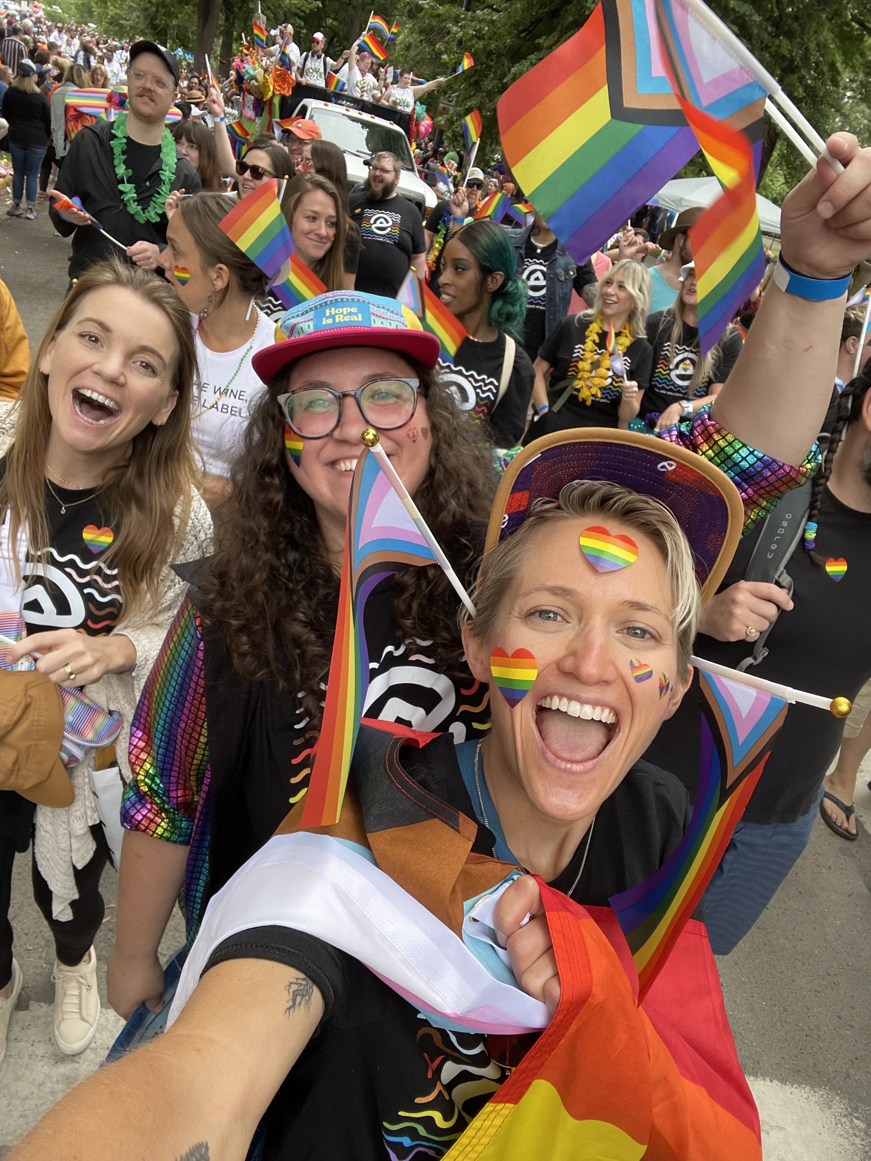 Evolve team members smile and celebrate at a Pride event. with rainbow attire and flags.