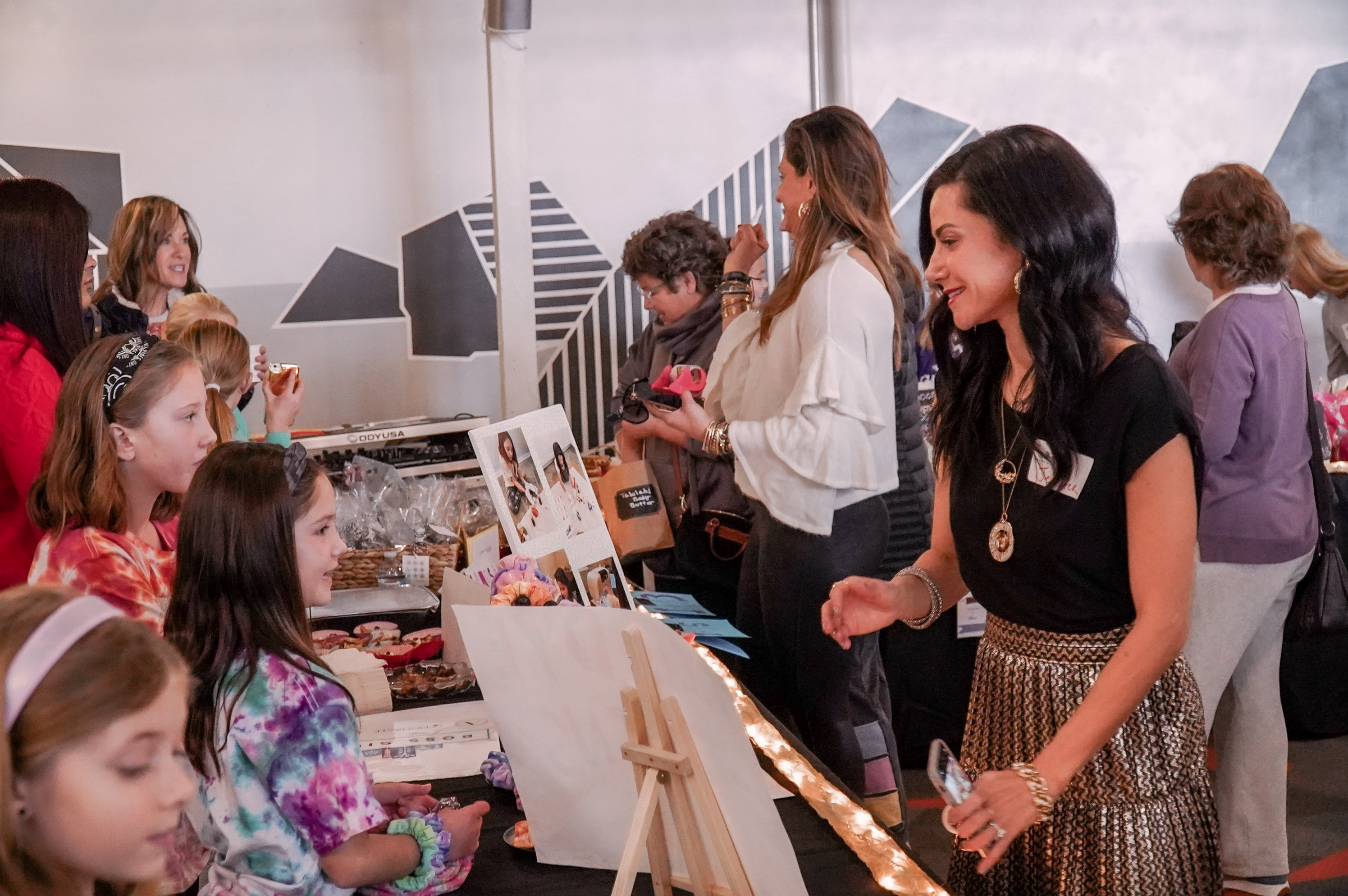 Treppie shop owners are young girls. This picture shows them standing at tables selling their work to Treppie founder Jennifer Andrews.