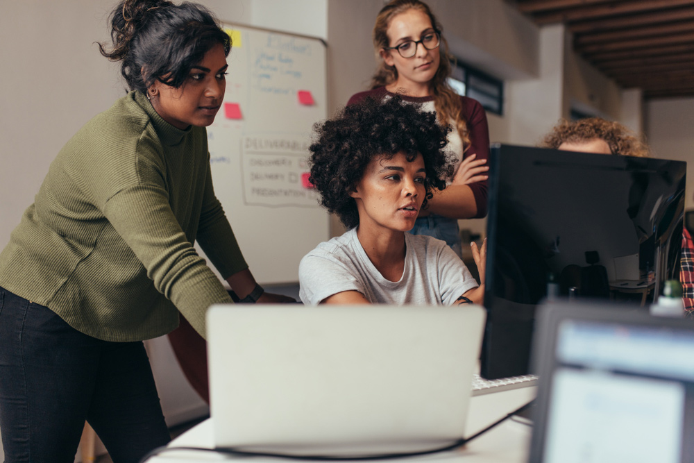 Woman programmer working on computer with colleagues standing by.