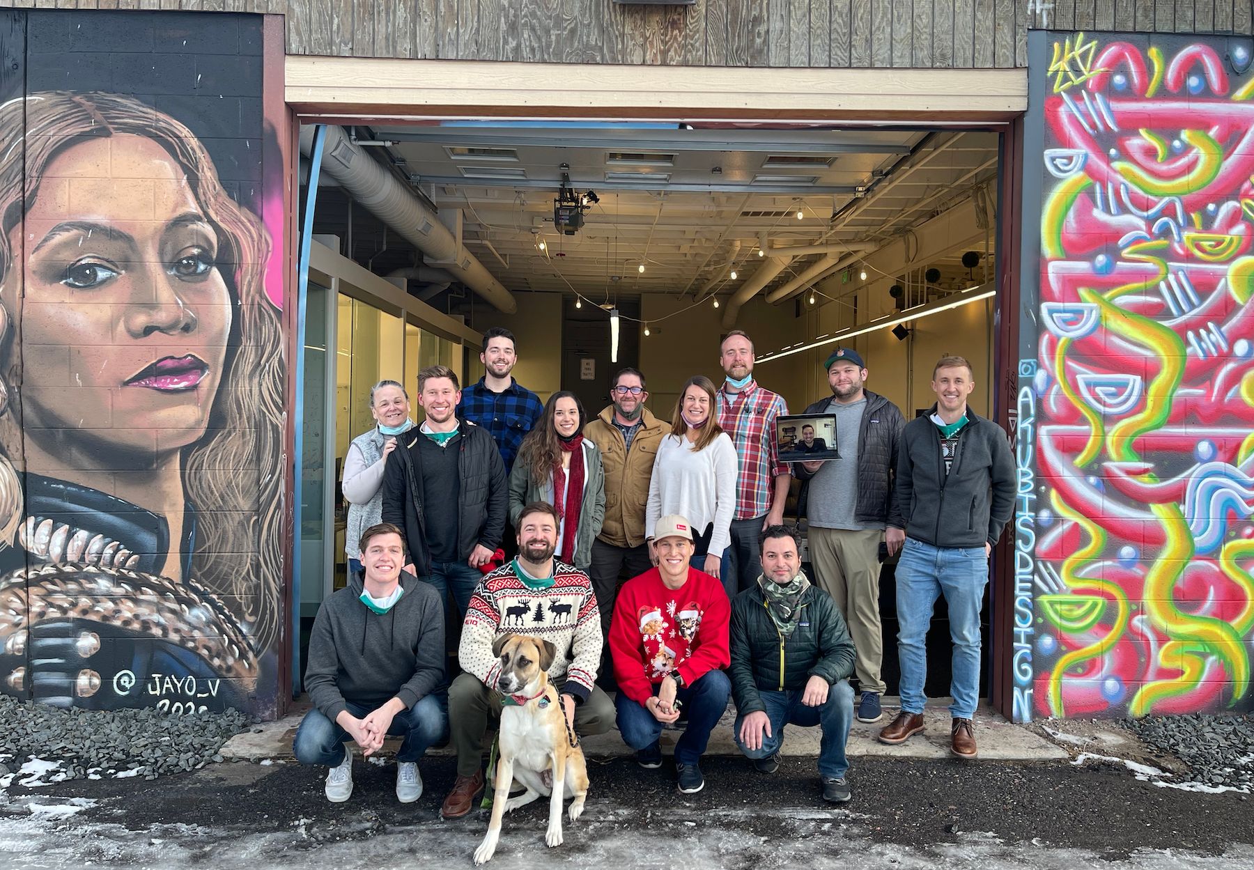 The team at Nomad poses for a photo during the holidays in front of a warehouse space with murals on each side 