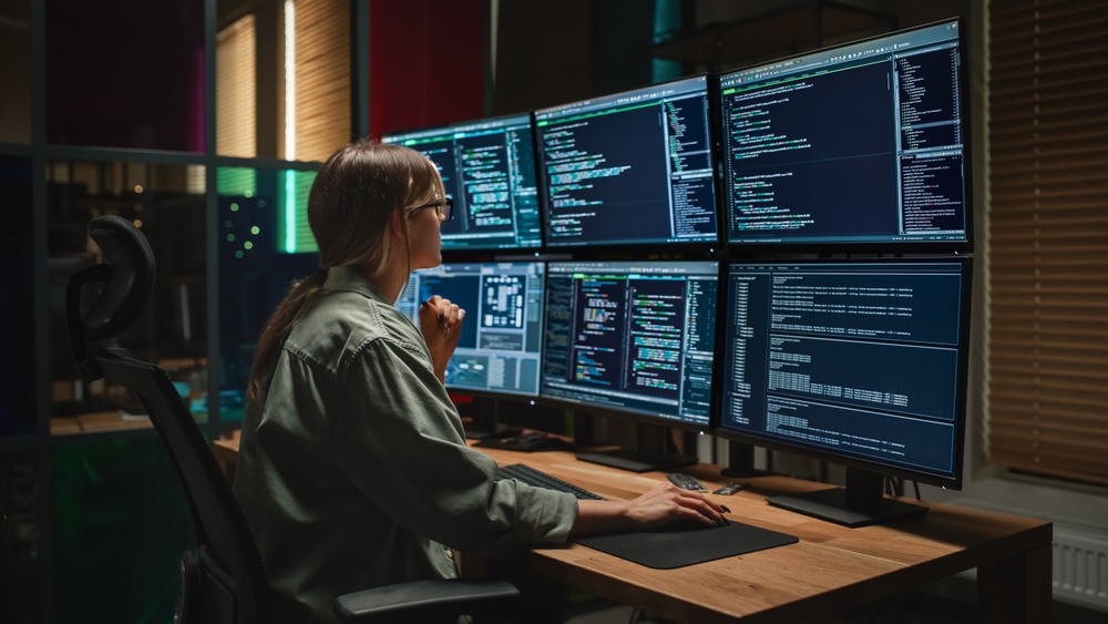 woman in front of a wall of computer monitors