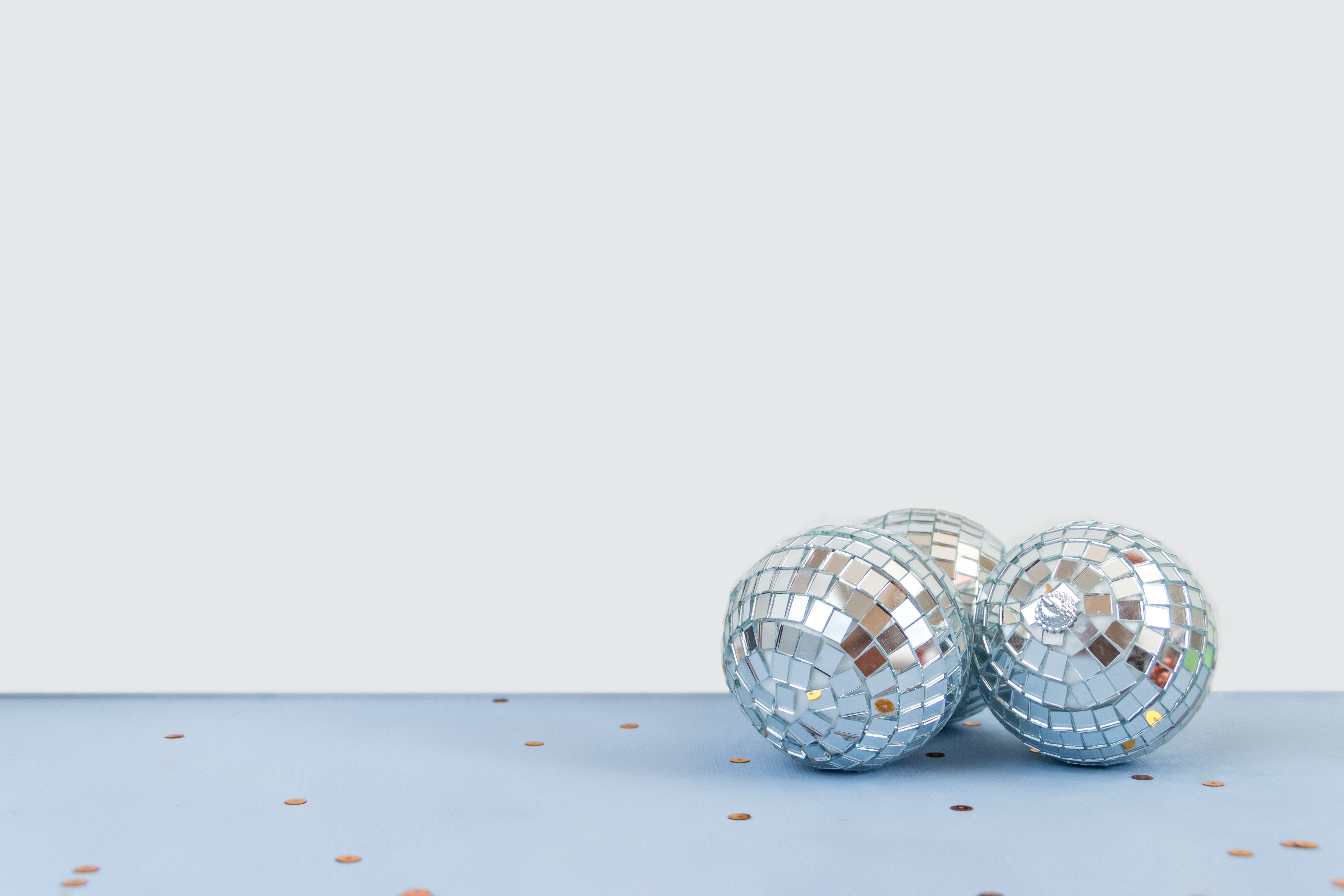 Image of three disco balls gathered together on a light blue floor against a white background