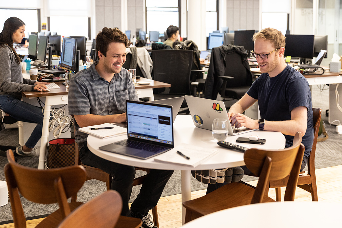 Two monday.com team members working on laptops together sitting at a table