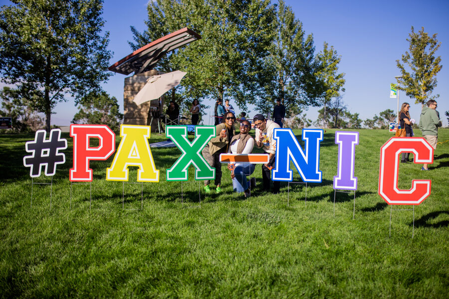 Multicolored yard sign at outdoor park reading “#PAX-NIC” with Pax8 team members posing next to it.