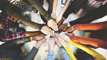 Several people standing in a circle with their hands in the center.