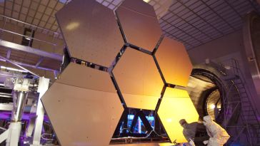 A scientist looking over several large, hexagonal panels of metal in a lab.