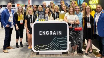 Engrain staff gather around a stand that says "Engrain" at a conference.