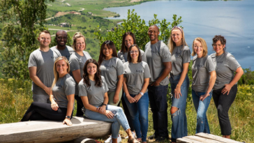 Tilt staff posing for a photo in front of a lake.