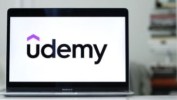 Udemy's logo on a laptop, resting on a gleaming desk.