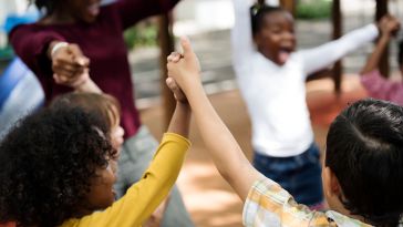  Photo of a circle of children holding raised hands and cheering 