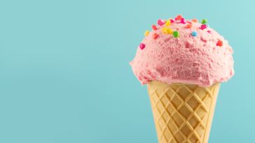  A pink ice cream cone with rainbow sprinkles on a mint green background. 