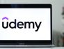 Udemy's logo on a laptop, resting on a gleaming desk.