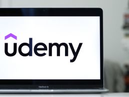 Udemy's logo on a laptop, resting on a gleaming desk.