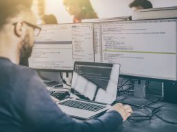 A developer writes code on a computer with multiple screens.